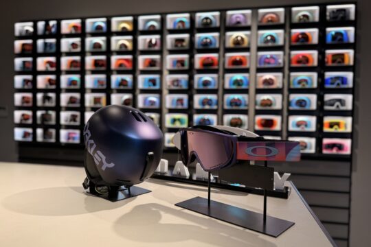 Photo du showroom Oakley Annecy-Le-Vieux avec fond flouté d'un mur de masques encastré lumineux et devant, exposition d'un casque et masque de ski